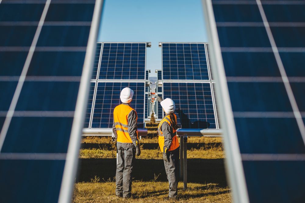 Homem e mulher com EPI's com diversas placas de energia solar em volta