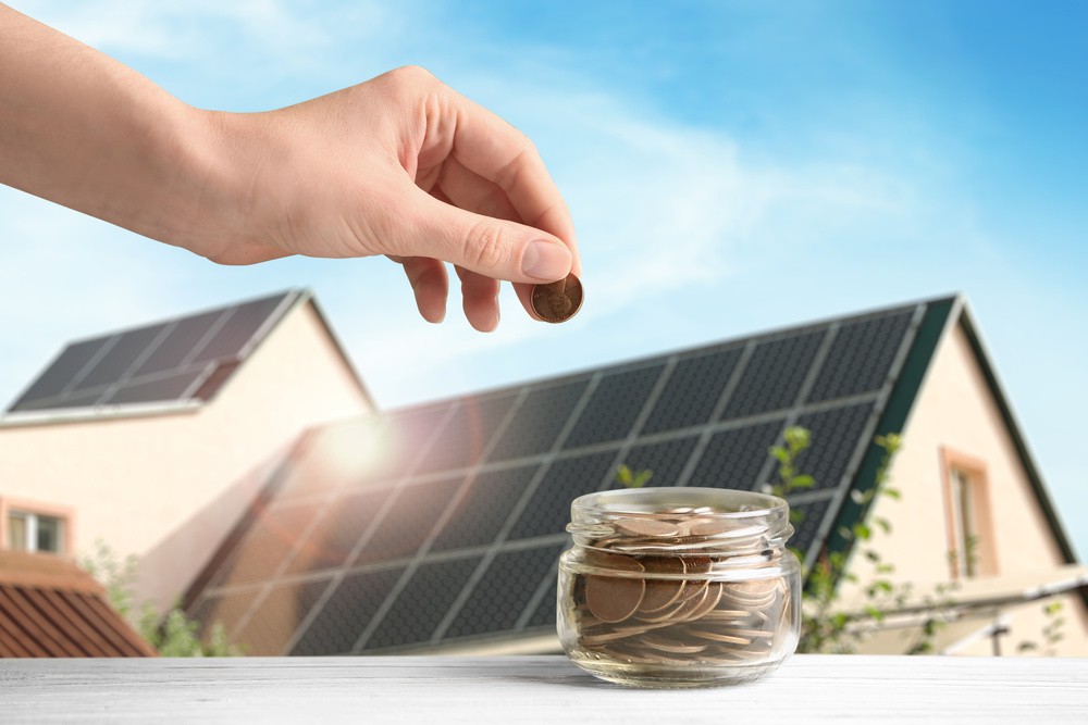 Pote de moedas e uma casa atrás com placas solares